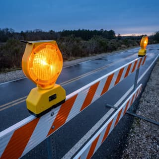 Illustration: a solar amber LED barricade light on a barricade closing an access road at dusk.