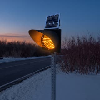 Illustration: a solar amber LED flashing beacon glowing beside a snowy country road after dark.