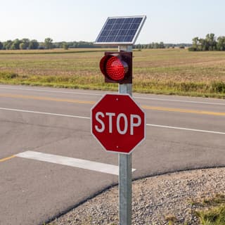 Illustration: a solar red LED flashing beacon mounted above a stop sign at a rural T-intersection.