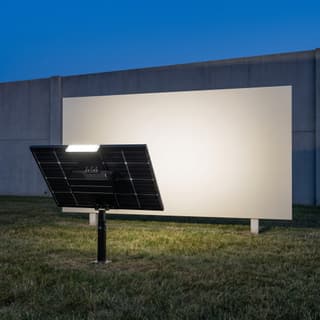 Illustration: a panel-on-post solar LED billboard uplight washing a blank monument sign at dusk.