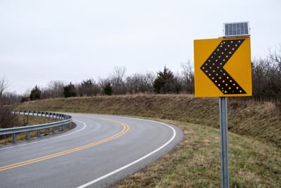 Illustration: a solar LED chevron alignment sign on the outside of a sharp bend on a rural highway.