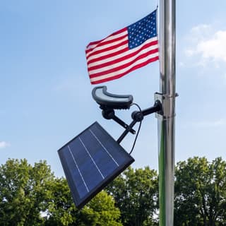 Illustration: a solar crescent LED flag pole light, switched off in daylight, clamped below the flag on a flagpole.