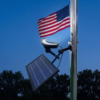 Illustration: a solar crescent LED flag pole light aiming its beam up a flagpole to light the flag at dusk.