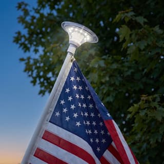 Illustration: a solar top-mount LED light on the tip of a residential flag pole lighting an American flag at dusk.