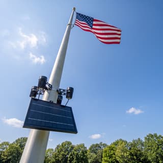 Illustration: a four-spot solar LED flag pole light, switched off in daylight, below an American flag.