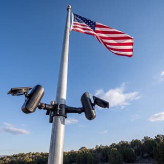 Illustration: a three-head solar LED flag pole light kit, switched off in daylight, below an American flag.