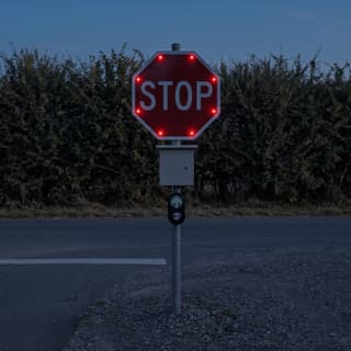 Illustration: a solar LED stop sign with a push button glowing at the exit drive of a rural county park lot after dark.