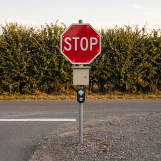 Illustration: a solar LED stop sign with a push button at the exit drive of a rural county park lot.