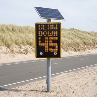 Illustration: a solar LED radar speed board showing SLOW DOWN and a driver's speed at a beach park entrance.