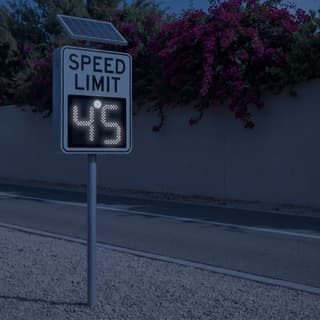 Illustration: a solar LED variable speed limit sign glowing the limit in white LEDs on a suburban road in a warm southwestern town after dark.