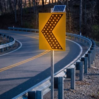 Illustration: a solar LED chevron alignment sign glowing at a sharp curve on a rural road after dark.