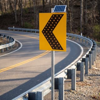 Illustration: a solar LED chevron alignment sign at the outside of a sharp curve on a rural road.