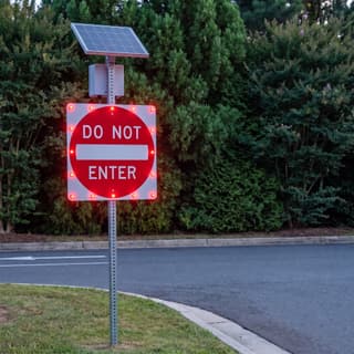 Illustration: a solar flashing do not enter sign glowing at a parking lot exit after dark.