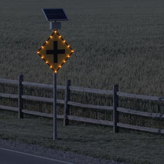 Illustration: a solar flashing intersection ahead sign glowing on a rural crossroads approach after dark.