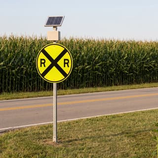 Illustration: a solar flashing railroad advance warning sign on a county road across open farmland.