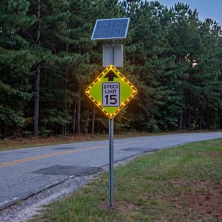 Illustration: a solar flashing reduced speed ahead sign with a speed limit plaque glowing at a campground entrance after dark.