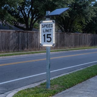 Illustration: a solar LED rectangle retrofit frame glowing around a speed limit sign on a residential street after dark.