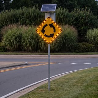 Illustration: a solar flashing roundabout warning sign glowing on a roundabout approach after dark.