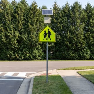 Illustration: a solar flashing school crossing sign at a marked crosswalk on a small-town street.