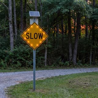 Illustration: a solar flashing SLOW sign glowing on a gravel campground lane after dark.