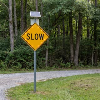 Illustration: a solar flashing SLOW sign on a gravel lane running into a campground.