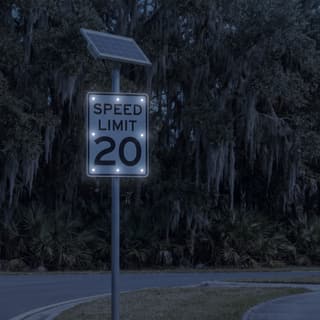 Illustration: a solar LED flashing 20 mph speed limit sign glowing on a residential street lined with live oaks after dark.