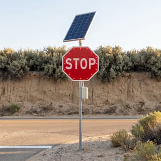 Illustration: a solar LED flashing stop sign with a lit border and lit letters at a remote desert junction.