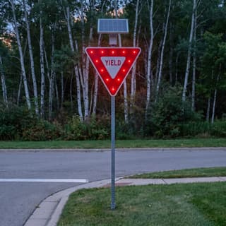 Illustration: a solar flashing yield sign glowing at a residential side-street junction after dark.