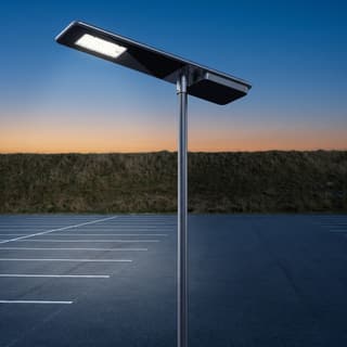 Illustration: a glossy black all-in-one solar LED lot light on a pole over a rural park-and-ride lot at dusk.