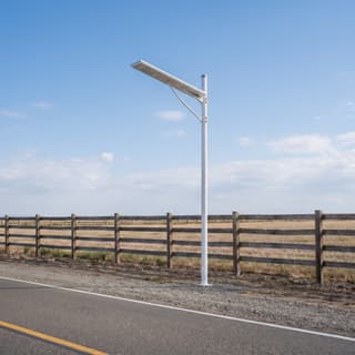 Illustration: a small solar LED light side-mounted on a pole, switched off and charging, at a gravel farm-lane turn-in in daylight.